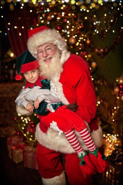 Nazik gülümseyen Noel Baba, elf kızını kollarına aldı. Noel ve Yeni Yıl masalları.