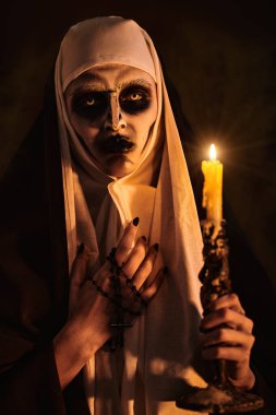 Korkunç şeytan ruhlu bir rahibe elinde mumla karanlık bir odada duruyor. Korku ve Cadılar Bayramı.