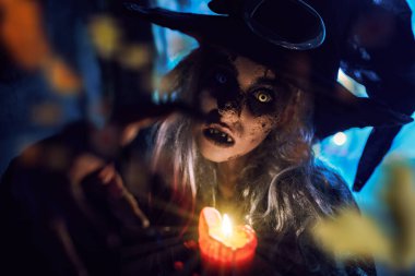 Cadılar Bayramı. Korkunç çirkin bir cadı elinde mumla terk edilmiş bir cadının ininde duruyor. Korkunç hikayeler.. 