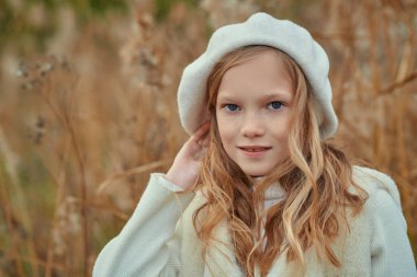 Sonbahar. Sonbahar parkında poz veren, kalın şapkalı ve kazaklı, gülümseyen küçük bir kızın portresi. Çocuk modası.