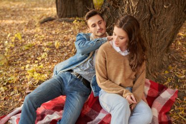 Sonbahar kot elbiseli güzel bir çift sıcak bir sonbahar gününde parkta bir ağacın altında dinleniyor. Aşk ve ilişki. 