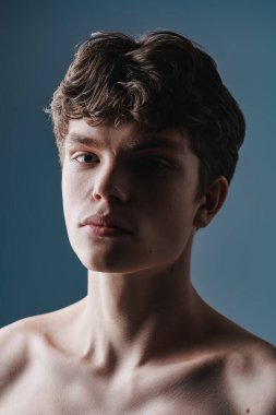 Çıplak omuzlu ve atletik yapılı yakışıklı bir gencin portresi. Stüdyo görüntüsü gri arka planda. Erkek güzelliği ve sağlığı. 