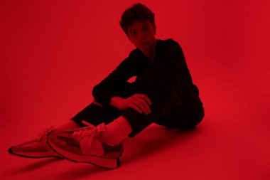 Yüzünde üzgün bir ifadeyle parlak kırmızı bir arka planda oturan yakışıklı bir adamın bacak fotoğrafı. Gençler ve akıl sağlığı. 