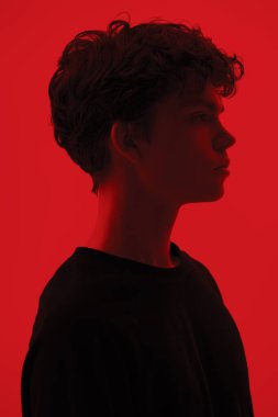 Dalgalı siyah saçlı, yüzünde depresif bir ifadeyle poz veren yakışıklı bir adamın portresi. Kırmızı arka planda stüdyo çekimi. İnsanlar, duygular. 