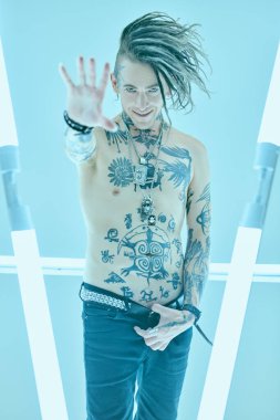 Modern bir punk rock müzisyeninin portresi. Havalı bir mohawk ile çıplak gövdesiyle sayısız dövmeyle poz veriyor. Gençlik alternatif kültürü. Mavi arkaplanda stüdyo resmi. 