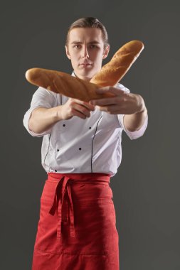 Genç profesyonel aşçı gri arka planda iki taze lezzetli baget tutuyor. Yemek ve yemek..