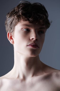 Kahverengi dalgalı saçlı, gömleksiz genç bir adamın stüdyo portresi. Erkek güzelliği ve sağlığı. Yakın çekim..