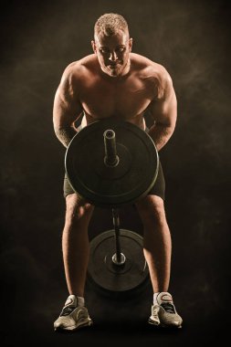 Yakışıklı kaslı adam koyu dumanlı arka planda halterle yoğun egzersizler yapıyor. Sağlık ve spor konsepti. Ağırlık kaldırma. Tam boy portre.