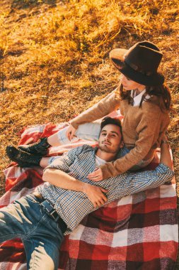 Romantik genç çift, nehrin kenarındaki battaniyenin üzerinde dinlenerek güneşli güzel bir günün tadını çıkarıyor. Aşk konsepti. Sonbahar mevsimi.