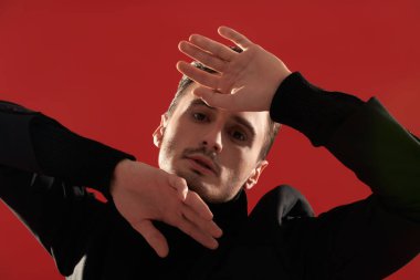 Kırmızı arka planda poz veren şık siyah elbiseli yakışıklı bir adamın stüdyo fotoğrafı. Erkek modası ve güzelliği.