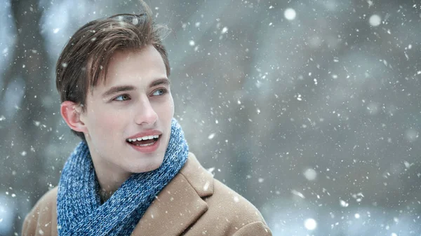 Modaya uygun ceketli ve eşarplı şık bir genç adamın portresi. Karlı bir günde, açık havada yürüyüş yaparken neşeyle gülümsüyor. Erkek güzelliği ve modası. Boşluğu kopyala.