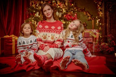 Örgü kazaklı güzel bir anne ve sevgili kızlarının portresi Noel arifesini aile çemberinde ve Noel ağacının yanında oturarak geçiriyor. Mutlu Noeller aile.. 