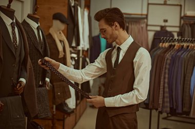 Zarif klasik takım elbiseli ve gözlüklü saygıdeğer bir işadamı kaliteli erkek giyim mağazasında uygun bir kemer seçiyor. Erkek modası, iş tarzı.. 