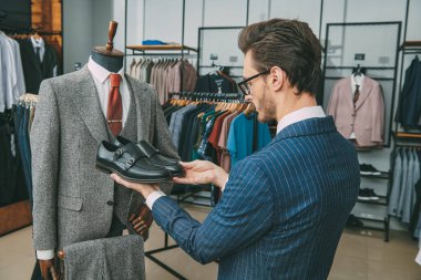 Erkek giyim mağazasından pahalı bir takım elbise için ayakkabı seçen saygın bir adamın portresi. Erkek modası ve tarzı.