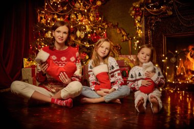 Güzel anne ve tatlı kızlarının portresi Xmas ağacı ve şöminenin yanında, içi hediyelerle dolu. Güzel dekore edilmiş oda arka planı. Mutlu Noeller aile.. 