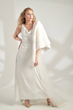 Pahalı bir gece elbisesi ve vizon peleriniyle kıvırcık sarı saçlı zarif genç bayan. Lüks bir şekilde. Güzellik, moda portresi. Gelinlik. Tam boy çekim.