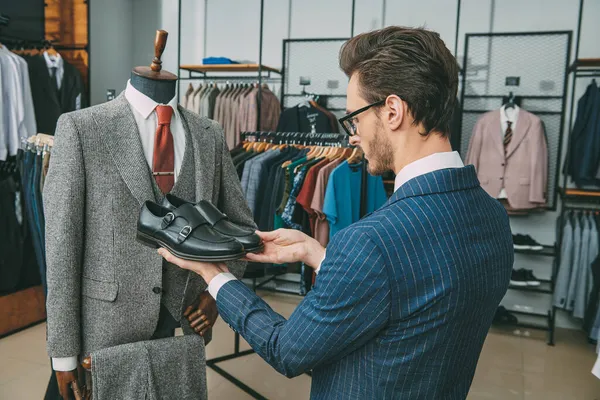 Erkek giyim mağazasından pahalı bir takım elbise için ayakkabı seçen saygın bir adamın portresi. Erkek modası ve tarzı.