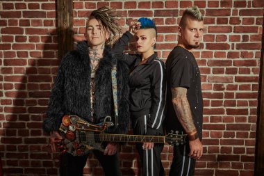 Gençlik alternatif kültürü. Siyah konser kostümleri içinde tuğla duvara karşı poz veren havalı punk rock müzisyenleri grubu. Grunge tarzı. 