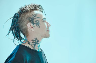 Siyah tişörtlü, gülümseyen ve başka tarafa bakan yakışıklı punk rock müzisyeninin yan görüntüsü. Mavi stüdyo geçmişi. Gençlik alternatif kültürü. Punk rock.