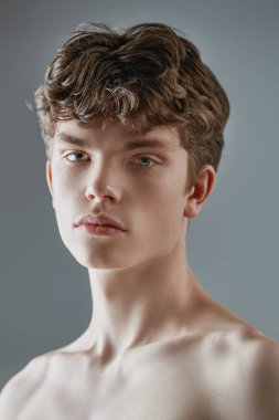 Kahverengi dalgalı saçlı, gömleksiz genç bir adamın stüdyo portresi. Erkek güzelliği ve sağlığı. Yakın çekim..