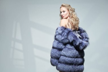 Kıvırcık sarı saçlı ve zarif makyajlı güzel ve şehvetli bir kadın pahalı bir gümüş tilki kürkü içinde poz veriyor. Kürk manto modası. 