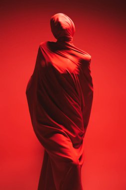 Yüksek moda ve sanat. Kırmızı kumaşa sarılmış etkileyici bir manken. Kırmızı arka planda tam boy stüdyo portresi.