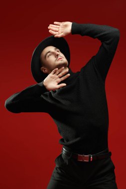 Siyah elbiseli ve kırmızı arka planda şapka takan etkileyici yakışıklı bir genç. Erkek modası ve tarzı. 
