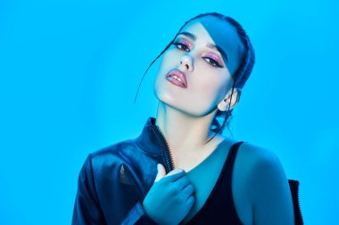 Güzellik, makyaj ve makyaj konsepti. Parlak akşam makyajı ve mavi bir arka planda poz veren parlak ışık demeti olan şehvetli esmer bir kızın portresi. Stüdyo çekimi. 