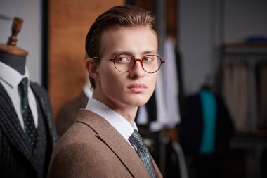 Zarif kahverengi takım elbiseli ve gözlüklü yakışıklı sarışın bir adamın portresi. Premium erkek giyim mağazasında duruyor. Erkek işi modası. Yakın çekim..