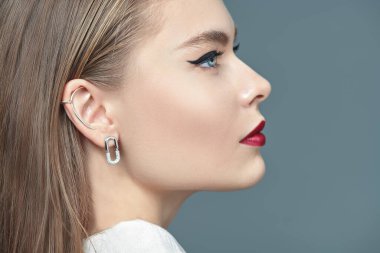 Gri stüdyo arka planında zarif makyajı ve takıları olan güzel sarışın bir kadın model. Makyaj ve saç stili. Portreyi kapat. 