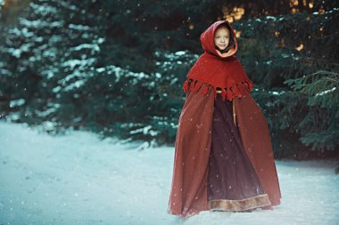 Sarı saçlı, açık mavi gözlü, ortaçağ kışlık giysileri giymiş mutlu bir kız güzel bir karlı ormanda yürüyor. Noel ve Yeni Yıl Masalları.