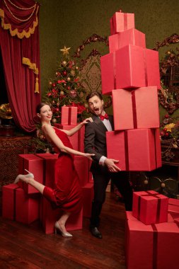 Güzel bir çift şık bir gece elbisesi içinde bir adam ve bir kadın lüks Noel süslemeleri içinde kırmızı hediye kutularıyla koşuyorlar. Noel ve Yeni Yıl indirimi, alışveriş.  