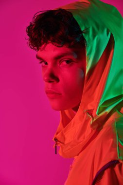 Gençlik tarzı ve yaratıcı tasarımcı kıyafetleri. Kafasında kapüşon olan parlak sarı ceketli havalı bir adamın moda fotoğrafı. Pembe arka planda stüdyo resmi.