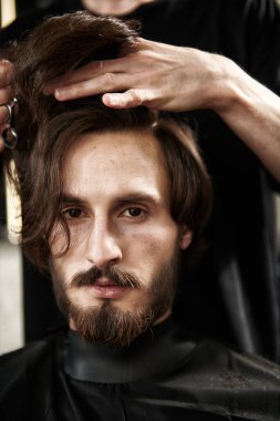 Sakallı, bıyıklı ve koyu renk saçlı yakışıklı bir genç berber dükkanında saçını kestiriyor. Berber dükkanı servisi. Yakın çekim..