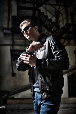 Siyah deri ceketli ve siyah güneş gözlüklü havalı adam şehrin eski semtinde caddede duruyor. Kentsel grunge tarzı. 