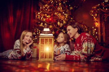 Noel 'in cazibesi. Mutlu anne ve küçük kızları şenlikli Xmas kazaklarıyla yerde uzanan ve pırıl pırıl altın ışıklara hayran olan muhteşem Noel atmosferinin tadını çıkarıyorlar..