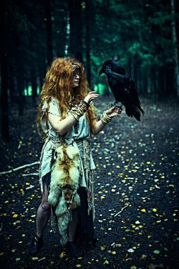 Cadılar Bayramı. Maskeli bir peri maskesiyle bir orman cadısı ormanın çalılıklarında duran siyah bir kuzgunla konuşuyor. Ölümün mistik ayini. Ayin kıyafetli kadın şaman..