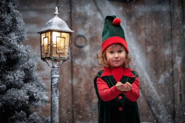 Küçük sevimli bir elf kızı kar taneleri yakalar ve sevinir. Tahta bir kulübede ve kar yağışı altında karla kaplı bir fenerde durur. Kış Noel Masalı.