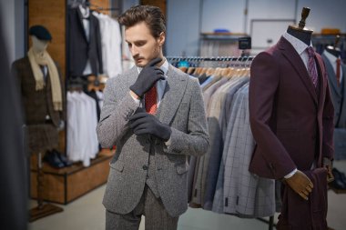 Yakışıklı, üç parçalı takım elbise giymiş esmer bir adam bir erkek giyim mağazasında yeni eldivenler deniyor. Erkeklerin iş modası.