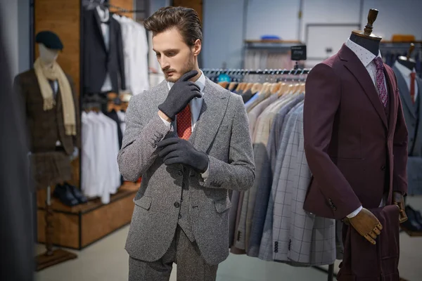 Yakışıklı, üç parçalı takım elbise giymiş esmer bir adam bir erkek giyim mağazasında yeni eldivenler deniyor. Erkeklerin iş modası.