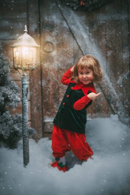 Kış Noel Masalı. Küçük sevimli bir elf kızı güler ve sevinir, kar yığınlarının arasında tahta bir kulübenin yanında durur ve karla kaplı bir fener kar altında kalır..