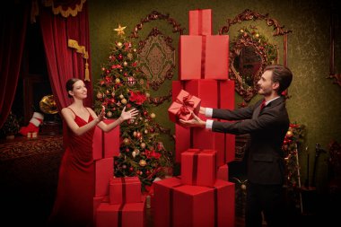 Noel ve yeni yıl alışverişi ve kutlaması. Zarif takım elbiseli neşeli bir adam lüks Noel iç dekorasyonu olan bir odada güzel kız arkadaşına hediye veriyor. Tatil modası. 