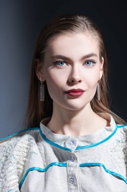 Güzellik ve moda çekimi. Zarif makyajlı ve düz saçlı güzel bir manken kız bej bir bluz içinde poz veriyor. Koyu gri arkaplanda stüdyo portresi.