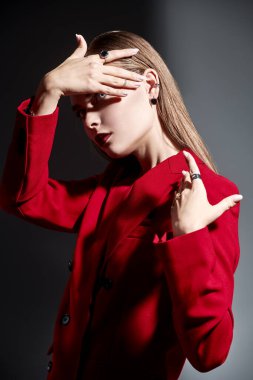 Zarif bir iş tarzı. Koyu gri arka planda gölgeli kırmızı pantolon giymiş zarif makyaj ve mücevherlerle poz veren güzel bir genç kadının portresi. Kadınlık, feminizm ve moda.