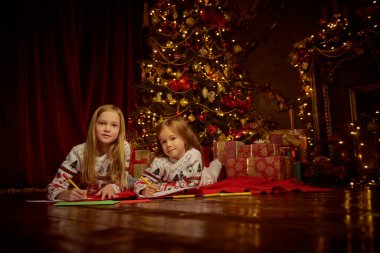 Noel 'de ve yeni yılda dilekler. İki küçük kız kardeş Noel arifesinde Noel Baba 'ya mektup yazıp evdeki rahat bir atmosferde Noel ağacının yanında yatıyorlar..
