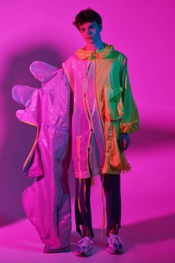 Yüksek moda çekimi. Parlak pembe arka planda siyah dalgalı saçlı şık tasarımcı kıyafetleriyle poz veren yakışıklı bir erkek modelin portresi. Tam boy çekim.