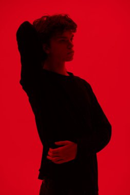 Dalgalı siyah saçlı, yüzünde depresif bir ifadeyle kırmızı arka planda dikilip dalgın dalgın bakan yakışıklı bir adamın portresi. Gençler ve duygular. 