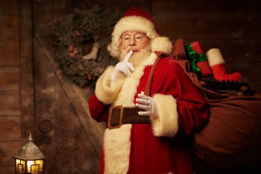 Noel Baba 'nın portresi büyük bir hediye çantasıyla gizlice bir evin yanında duruyor parmağını dudaklarına dayayıp varlığını belli etmemesini istiyor. Mutlu Noeller ve mutlu yıllar.! 