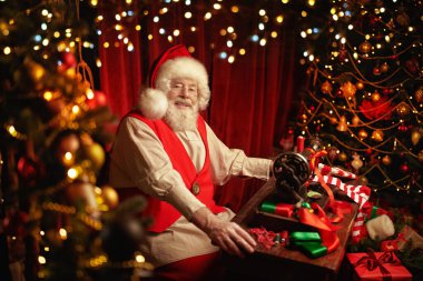 Mutlu gülümseyen Noel Baba atölyesinde Noel çorapları dikiyor. Noel Baba 'nın rahat atölyesi Noel ağaçları ve ışıklarla süslenmiş. Noel gelenekleri ve peri masalları. 