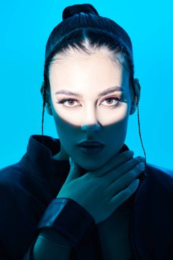 Güzellik, makyaj ve makyaj konsepti. Parlak akşam makyajı ve mavi bir arka planda poz veren parlak ışık demeti olan şehvetli esmer bir kızın portresi. Stüdyo çekimi. 